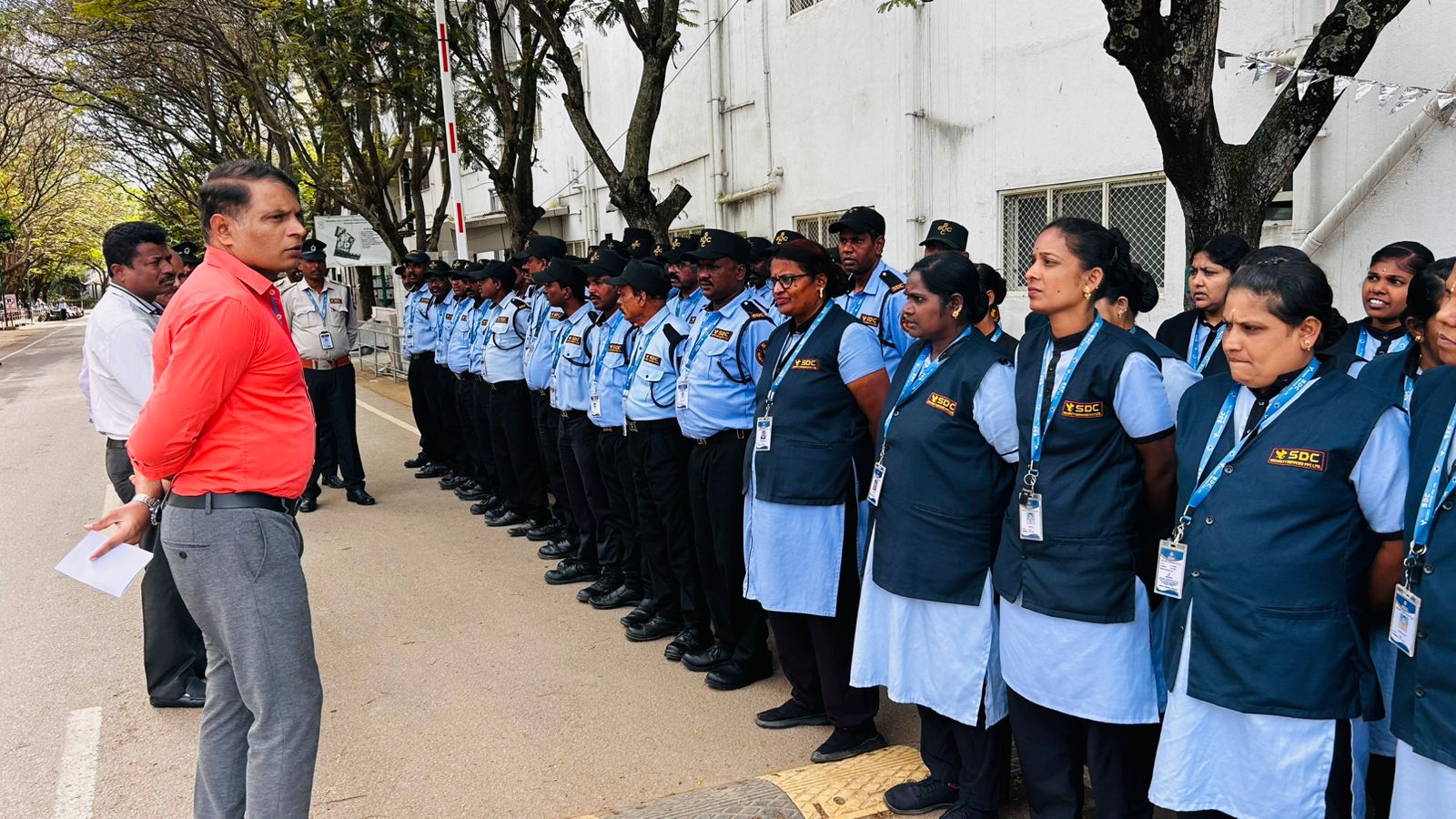Supervisor briefing SDC guards and housekeeping staff at a site gate